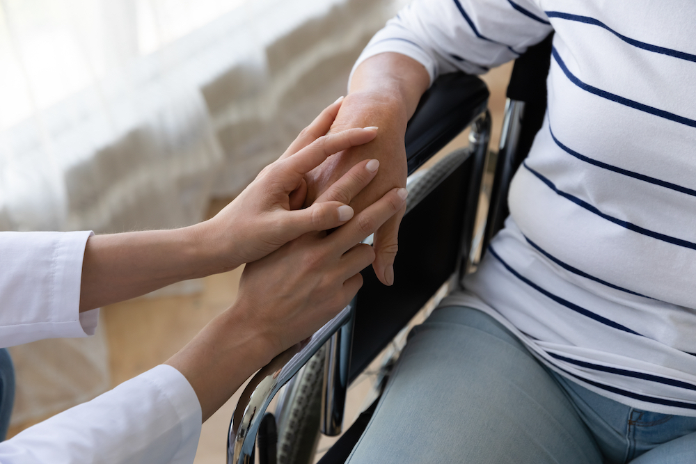 A nurse touches the hand of a senior woman in a wheelchair