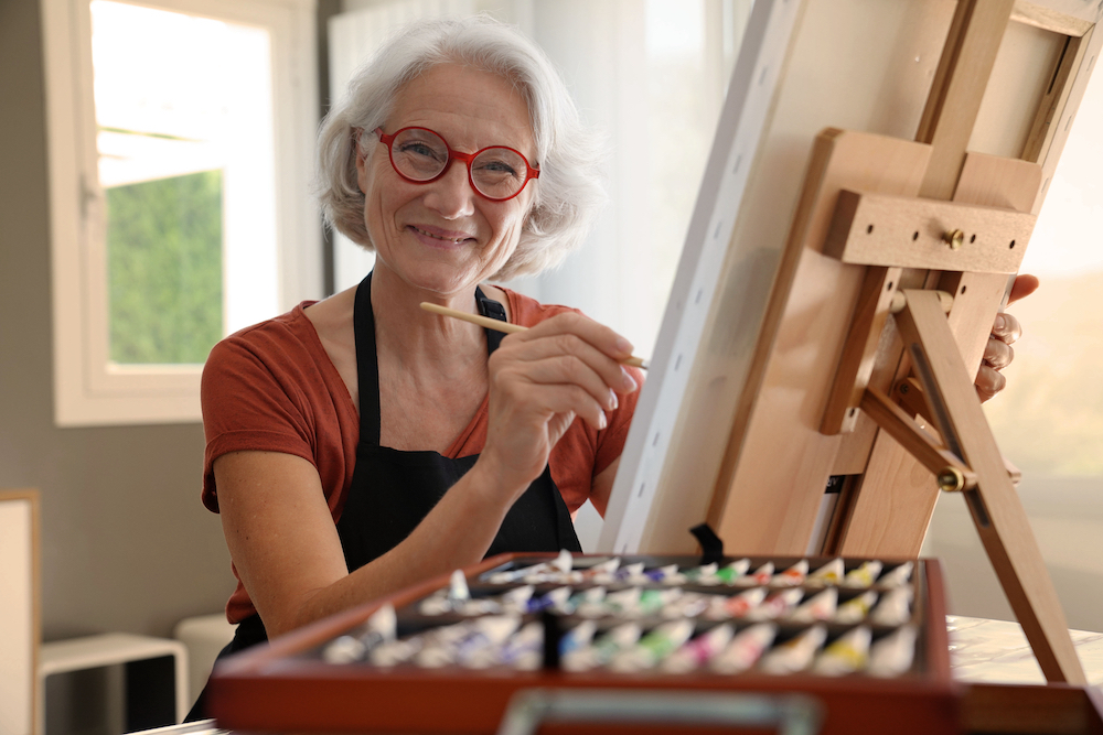 A senior woman paints on a canvas