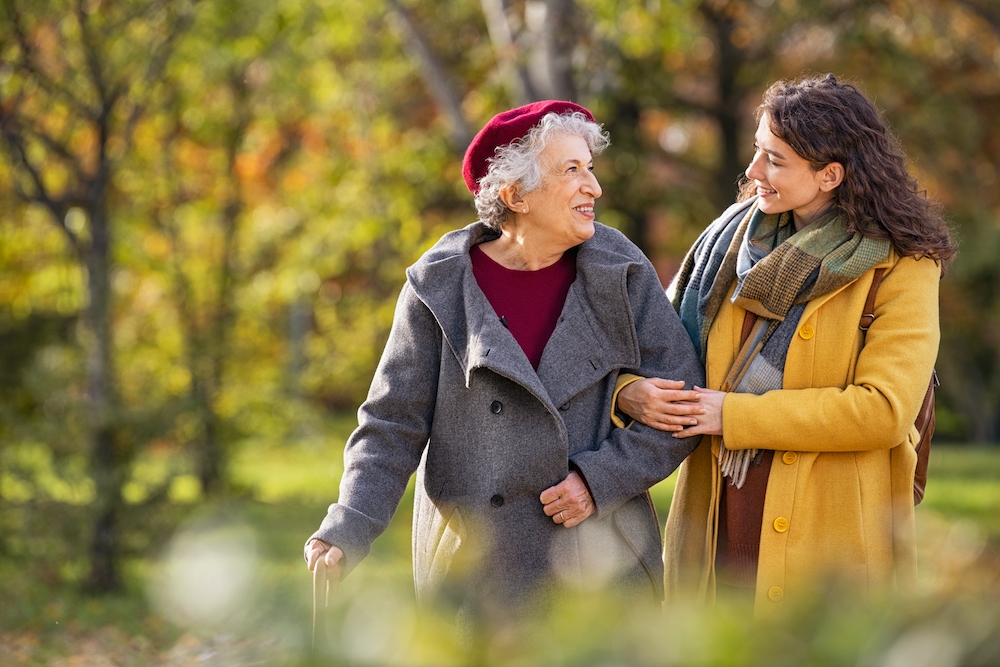 A caregiver and a senior woman walk through the park together